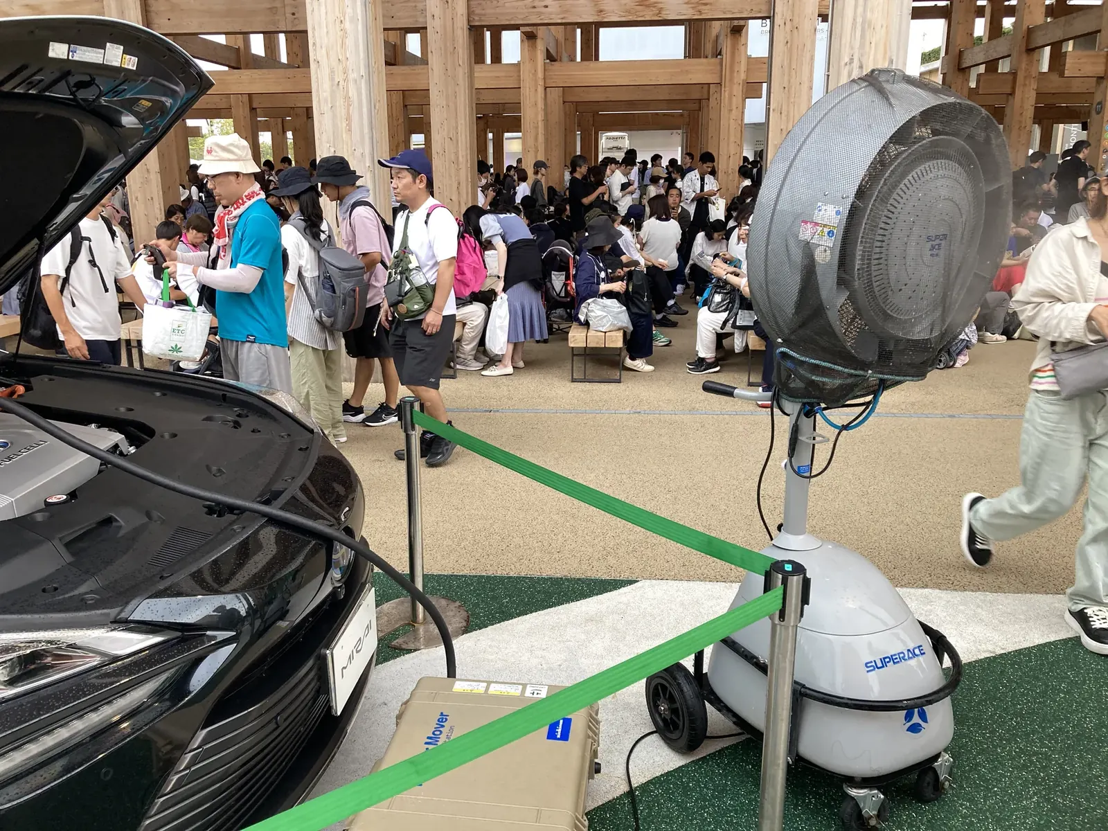 ミスト扇風機と電気自動車展示の周りで休む人々