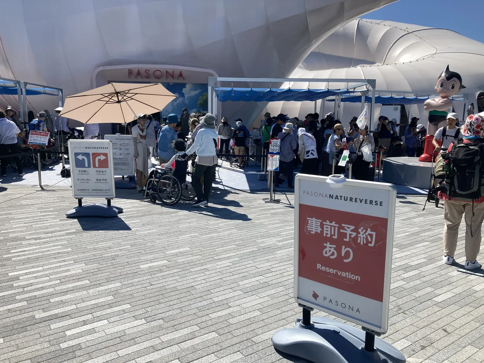 PASONA NATUREVERSE 前に並ぶ家族と、横で見守るアトムの像
