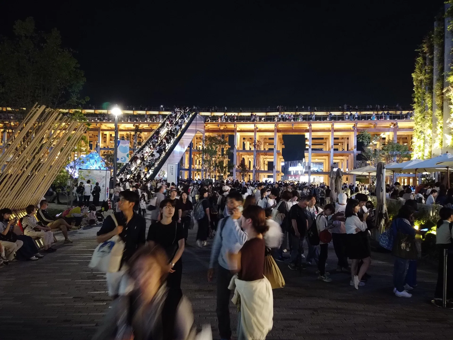 夜の大屋根リング、階段にぎっしり並んだ観客と、その下の広場を歩く来場者の群れ（俯瞰）