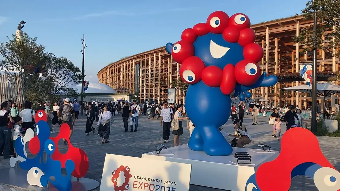 大阪・関西万博の会場広場に立つミャクミャク像と、背後の大屋根リング